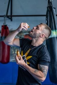 Athletic man in gym holds CBD oil, emphasizing fitness and wellness.