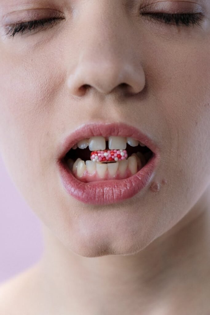 A woman with eyes closed holding a red and white capsule between her teeth in a close-up shot.