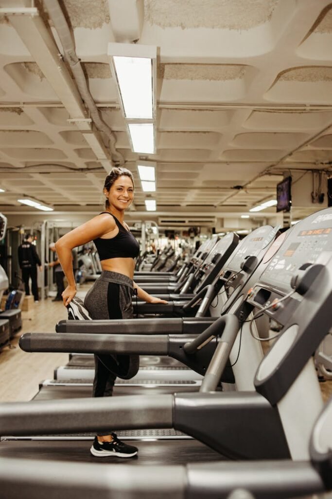 Smiling woman stretching on a treadmill in a gym setting, promoting a healthy lifestyle.