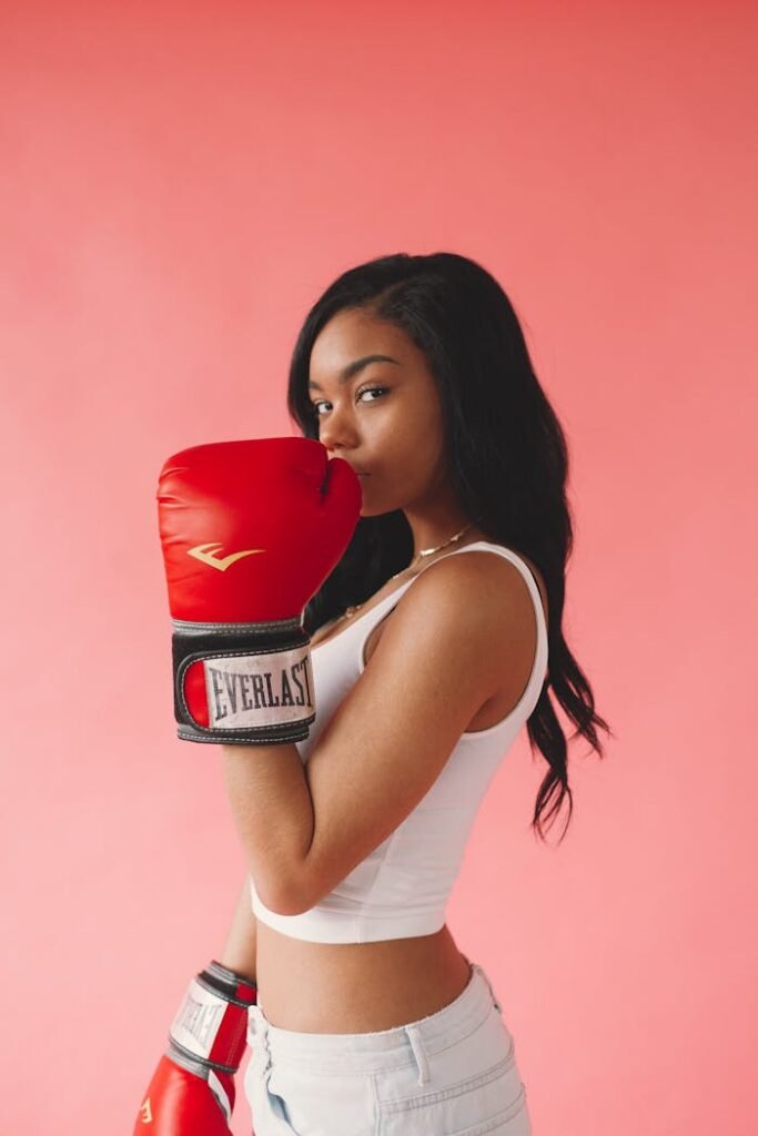 Stylish woman posing with red boxing gloves on a pink background, exuding confidence and fitness.