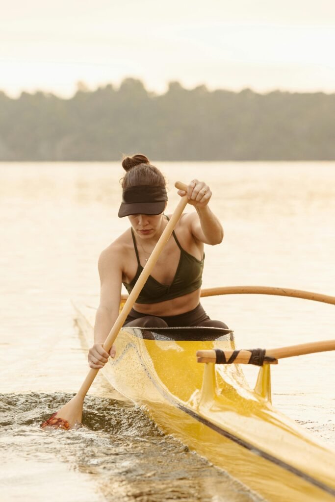 A woman paddles a yellow canoe across a calm lake during the day, embracing outdoor recreation.